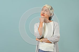 Thoughtful senior woman thinking and looking up expressing doubt and wonder isolated blue background