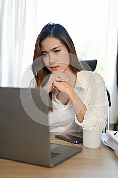 Thoughtful serious Asian businesswoman working at her modern office desk