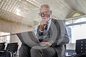 Thoughtful serious businessman using laptop while sitting at subway or railroad train station building