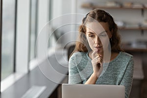 Thoughtful serious gen Z student girl using laptop at home