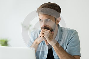 Thoughtful serious man lost in thoughts in front of laptop