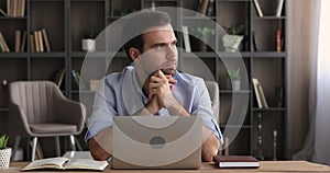 Thoughtful serious man sit at table working on laptop