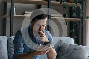 Thoughtful serious man touching chin, looking at smartphone screen