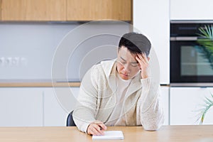 Thoughtful serious young asian man looking away. student writer sit at home office desk with laptop thinking of inspiration search