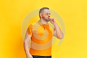 Thoughtful smart serious man standing and thinking a lot with finger on chin over yellow background