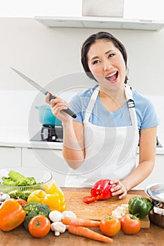 Thoughtful smiling woman chopping vegetables in kitchen