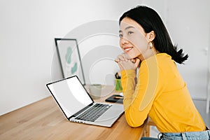 Thoughtful smiling young woman with laptop looking away sitting at home office