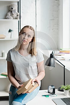thoughtful teen student girl with books sitting on work desk