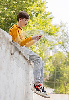 Thoughtful teenager boy resting. Holding and using a smartphone for networking on a sunny day, outdoors.
