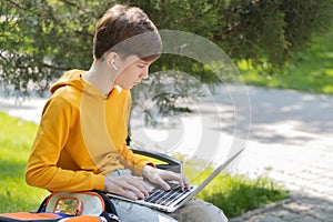 Thoughtful teenager boy working on laptop. Holding and using a laptop for networking on a sunny spring day, outdoors.