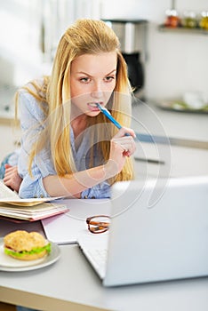 Thoughtful teenager girl studying in kitchen