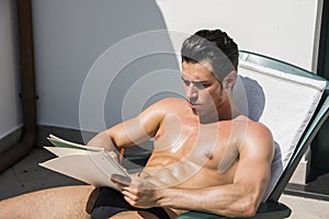 Thoughtful topless young man in deckchair with pencil and notebook