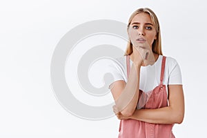 Thoughtful and troubled young concerned blond woman thinking about something concerning, hold hand under chin, frowning