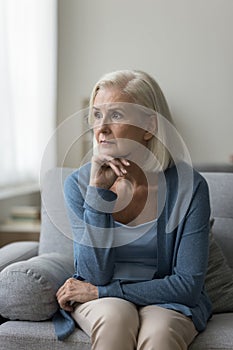 Thoughtful upset middle-aged woman sit on sofa at home