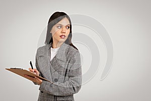 Thoughtful woman with clipboard on grey background, free space