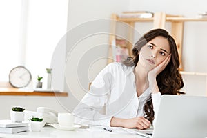 Thoughtful woman with hand under chin bored at work, looking away sitting near laptop, demotivated office worker feels