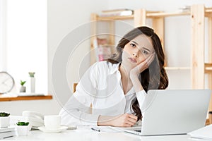 Thoughtful woman with hand under chin bored at work, looking away sitting near laptop, demotivated office worker feels