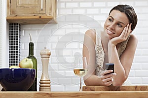 Thoughtful Woman Holding Cellphone While Leaning On Wooden Counter