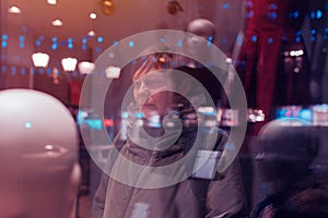 Thoughtful woman looking through shop window at night