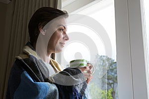 Thoughtful woman looking through window while having cup of coffee