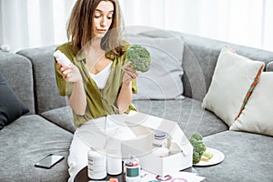 Thoughtful woman with nutritional supplements and broccoli at home