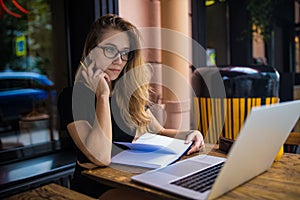 Thoughtful woman with pensive look in spectacles skilled real estate analyst reading information on website via laptop computer