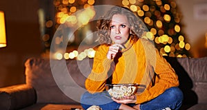 Thoughtful woman with popcorn watching movie at night