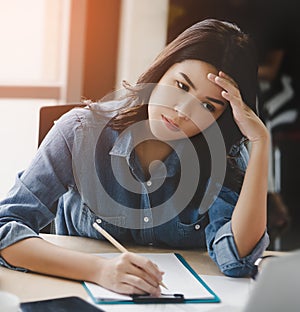 Thoughtful woman with serious expression writing down note from laptop computer in office