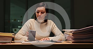 Thoughtful woman sits at desk littered with documents