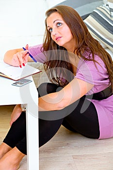Thoughtful woman sitting on floor and making notes