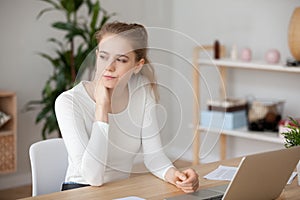 Thoughtful woman sitting in front of laptop, lost in thoughts