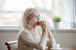 Thoughtful woman sitting at table with cup of tea