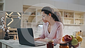 Thoughtful woman working laptop sitting kitchen close up. Girl making notes.