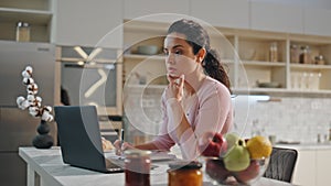 Thoughtful woman working laptop sitting kitchen close up. Girl making notes.