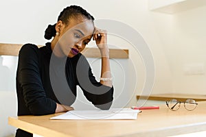 Thoughtful worried African or black American woman holding her forehead with hand looking at notepad in office