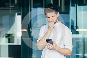 Thoughtful and worried young man, businessman, freelancer looks at the phone, received bad news
