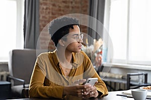 Thoughtful young African American businesswoman holding cellphone in hands.