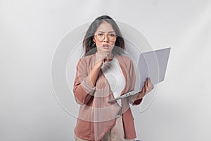 Thoughtful young Asian business woman in eyeglasses with a laptop thinking about work, isolated by white background