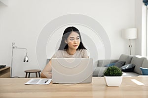 Thoughtful young Asian freelance business woman sitting at laptop