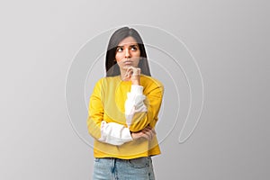 thoughtful young attractive multi ethnicity woman in trendy yellow sweater against light grey background holding her