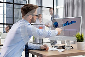 Thoughtful young business man in shirt working using computer while sitting in the office with collegues on the