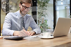 Thoughtful young business man writing something down while working in modern office