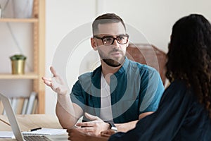 Thoughtful young businessman in glasses discussing project with biracial colleague.