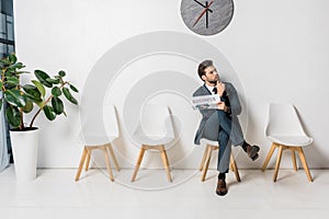 thoughtful young businessman holding newspaper and waiting