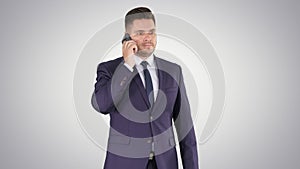 Thoughtful young businessman in suit and tie making several calls quickly on gradient background.