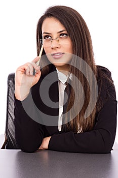 Thoughtful young businesswoman sitting at her desk holding a pen