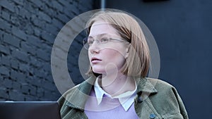 Thoughtful young businesswoman typing on laptop outside in street cafe