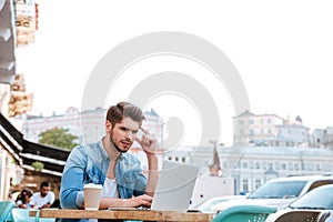 Thoughtful young casual man looking at laptop in cafe outdoors
