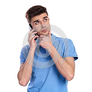 Thoughtful young casual man talking on the phone looks up