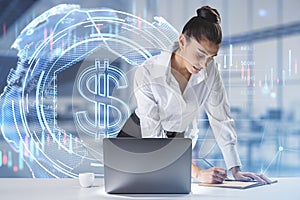 Thoughtful young european businesswoman leaning and writing on desktop with laptop and glowing dollar hologram on bright blurry